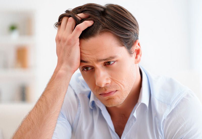 Молодой мужчина в светло-голубой рубашке сидит в светлой комнате, держа руку в волосах